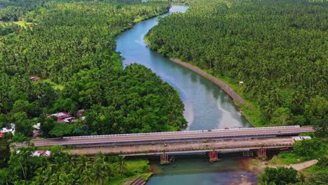 Panoramablick-Auf-Den-Von-üppigen-Kokospalmen-Gesäumten-Fluss-Und-Die-Ländliche-Brücke-In-Saint-Bernard,-Southern-Leyte,-Philippinen---Luftaufnahme