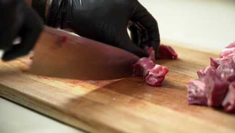 Chef-is-dicing-the-most-delicious-fresh-chuck-of-beef,-using-black-gloves-and-sharp-chef-knife
