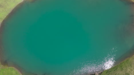 Downward-angle-and-rising-drone-shot-of-the-turquoise-water-of-Oreti-Lake-in-Tusheti-Georgia