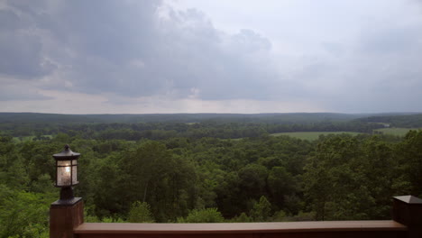 Push-out-from-the-deck-of-a-large-out-towards-trees,-green-fields,-forest-and-hills-beyond-on-a-cloudy-summer-evening-in-southern-Missouri