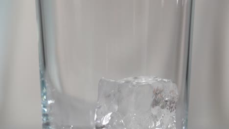 Macro-ice-cubes-being-dropped-into-clear-tall-glass-with-white-background-slow-motion-4k
