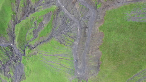 Cinematic-downward-angle-drone-shot-of-vehicle-driving-on-steep-cliffs-on-the-Road-to-Tusheti,-one-of-the-worlds-most-dangerous-roads