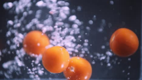 Cherry-Tomatoes-dropping-in-slow-motion,-fruits-floating-in-water-on-black-background