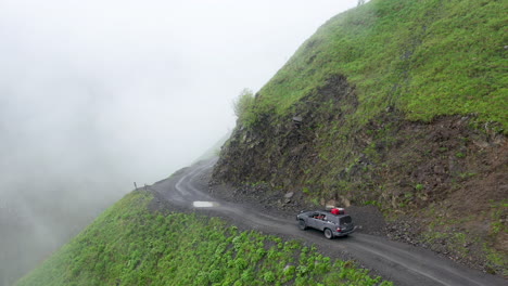 Cinematic-drone-shot-of-vehicle-driving-on-the-edge-of-a-cliff-on-the-Road-to-Tusheti-going-through-puddles,-one-of-the-worlds-most-dangerous-roads