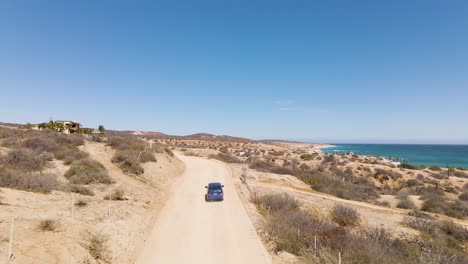 Aerial:-car-driving-on-winding-dirt-road-on-Mexican-coastline,-tracking-shot