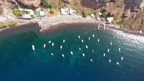 Static-aerial-top-down-view-of-many-fishing-boats-in-the-Mediterranean-Sea-with-crytal-clear-blue-water-and-beach-Santorini,-Greece