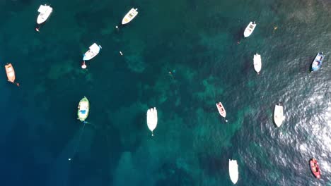Top-down-view-of-fishing-boats-in-the-Mediterranean-Sea-with-crytal-clear-blue-water-revealing-in-Santorini,-Greece