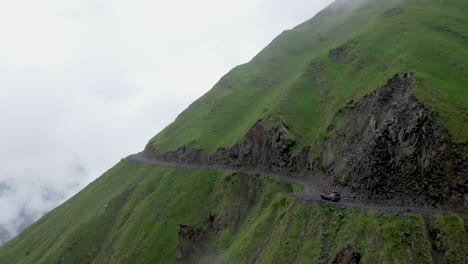 Cinematic-drone-shot-of-vehicle-driving-on-the-edge-of-a-cliff-on-the-Road-to-Tusheti,-one-of-the-worlds-most-dangerous-roads