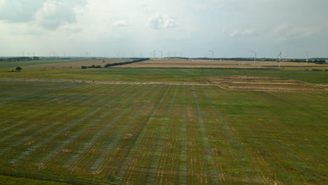 Vast-Green-Fields-For-Solar-Panel-Farm-With-Wind-Turbines-In-Background-Near-Zwartowo-In-Poland