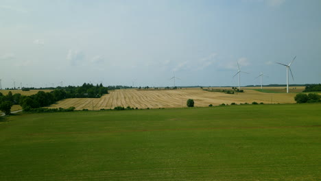 Beautiful-rural-landscape-with-a-view-of-a-mown-field-with-corn-stubble-and-windmills-spinning-in-the-wind,-harvesting-shot-by-Aerial-shot,-Poland