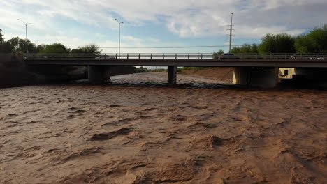 Drone-View-Of-Raging-River-After-Monsoon-Storm-With-Brown-Water-Flowing-Under-Road-Bridge