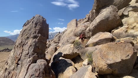 Female-With-Backpack-on-Hiking-Trail-in-Alabama-Hills,-California-USA-on-Hot-Day-Walking-on-Hill-Between-Rocks,-Panoramic-Full-Frame-Slow-Motion