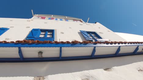 Umkreisende-Aufnahme-Eines-Weißen-Gebäudes-Mit-Blauem-Fensterrahmen-Und-Einem-Leeren-Restaurant-Am-Meer,-Das-In-Bodrum-Speist