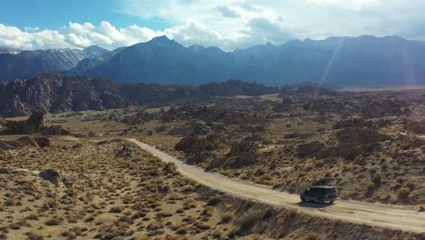 Dark-Van-on-Desert-Road,-Cinematic-Tracking-Aerial-View-of-Vehicle-Moving-in-Dry-Landscape-of-Alabama-Hills,-California-USA