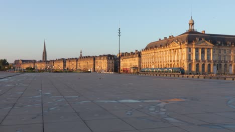 Sunrise-at-the-water-mirror-in-Bordeaux-with-nobody-in-sight-and-tramway-in-the-background,-slow-wide-pan