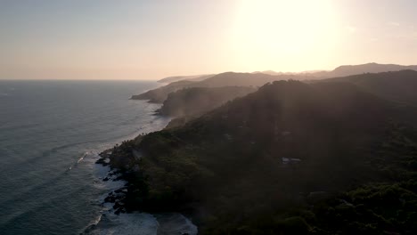 Picturesque-aerial-shot-of-Coastline-alongside-Cliffside-with-Pacific-Ocean-Water-following-the-Sun-rays-During-Sunset