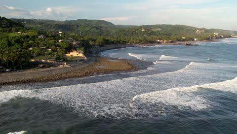 Aerial-shot-of-ocean-waves-crashing-the-coastline,-El-Tunco-beach-in-El-Salvador,-tourism-and-surfing