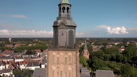 Closeup-and-approach-aerial-view-of-tower-of-the-Walburgiskerk-cathedral-in-medieval-Hanseatic-town-of-Zutphen-in-The-Netherlands-with-the-Drogenapstoren-and-wider-town-cityscape-in-the-background
