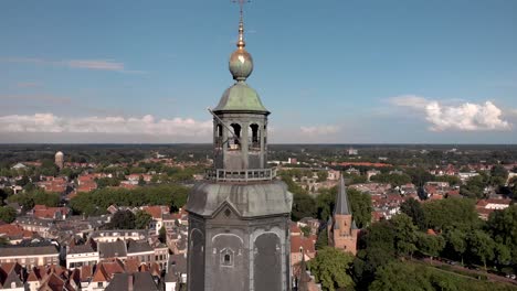 Ascend-aerial-of-the-Walburgiskerk-cathedral-with-golden-weathercock-in-medieval-Hanseatic-town-Zutphen-in-The-Netherlands-showing-Drogenapstoren-and-watertower-behind-in-flat-Dutch-landscape