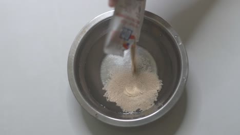 Adding-active-instant-dry-yeast-into-a-bowl-of-warm-water,-slow-motion-video-clip