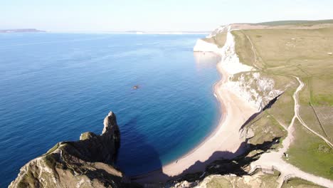 Aerial-View-Of-Sunny-Empty-Beach-Beside-Rolling-Hill-Cliffs-At-By-Durdle-Door-In-Dorset