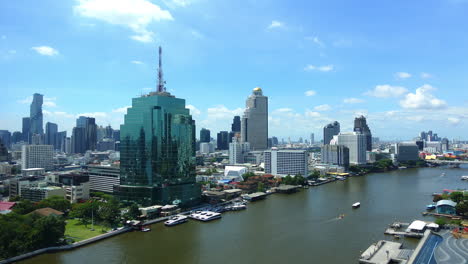 Daytime-Timelapse-of-Boats-and-ships-moving-along-Chao-Phraya-river-with-high-skyscrapers-buildings-like-Cat-Tower-Bangkok-and-Lebua-State-Tower-on-the-river-banks,-cityscape-panorama