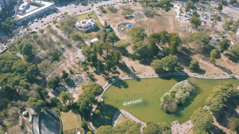 AERIAL---Centenario-Park-and-its-lake,-Buenos-Aires,-Argentina,-spinning-shot