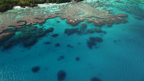 Slow-tilt-up-above-crystal-water-revealing-Maré-coastline,-New-Caledonia---aerial