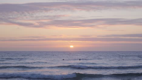 Zwei-Surfer,-Die-Die-Untergehende-Sonne-Beobachten,-Während-Sie-In-Portugal-In-Den-Wellen-Schwimmen
