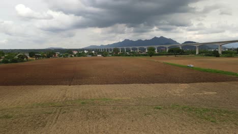 4K-Aerial-dolly-out-shot-capturing-the-large-piece-of-newly-tilled-agriculture-farmland-with-Muak-Lek-mountains-in-the-background-and-high-speed-train-line-across-the-frame