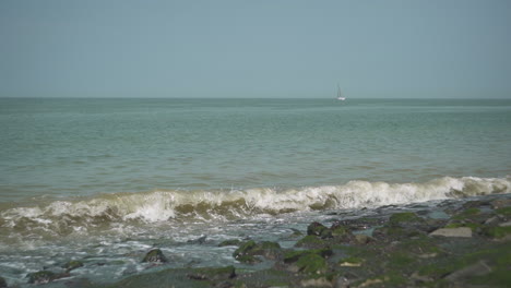 Wellen-An-Der-Küste-Mit-Einem-Segelschiff-Im-Hintergrund,-Zeitlupe