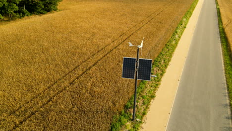 Windgenerator-Und-Sonnenkollektorsystem-Auf-Beleuchtungsmast-In-Der-Nähe-Von-Gelbem-Weizenfeld-Und-Asphaltierter-Straße-Auf-Dem-Land