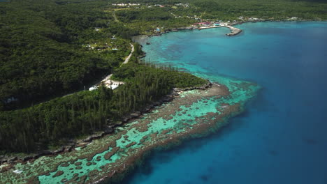 Aerial-ascending-shot-revealing-amazing-coral-bay-beach-and-Tadine-wharf,-on-Maré-Island,-New-Caledonia