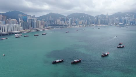 Konvoi-Lokaler-Fischerboote,-Die-In-Hongkong-Victoria-Bay-Verursachen,-Mit-Der-Skyline-Der-Stadt-Am-Horizont,-Luftbild