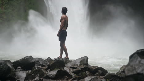 Rising-shot-of-man-standing-in-front-of-powerful-La-Fortuna-jungle-waterfall