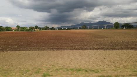 Artistic-contrast-aerial-footage-spilt-into-three-parts-horizontally,-unplowed-land,-tilled-farmland-beautiful-mountains-and-a-looming-rainclouds-in-sky-in-Muak-Lek,-Saraburi,-Thailand