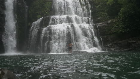 Wide-shot-panning-up-to-man-at-base-of-Nauyaca-waterfalls-in-Costa-Rica