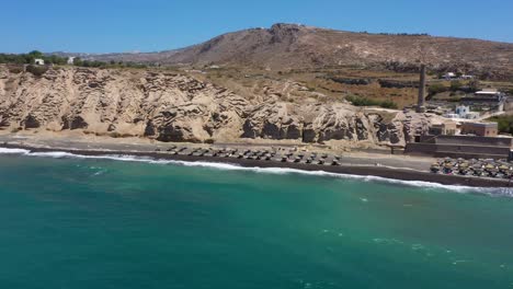 Antena-De-Isla-Griega,-Acantilados-Rocosos-Y-Olas-De-Agua-Azul-En-El-Mar-Mediterráneo-En-Playa-Blanca-En-Santorini,-Grecia