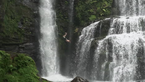 Shot-following-man-as-he-does-backflip-off-jungle-waterfall,-slow-motion
