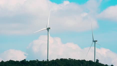 Dolly-Out,-Saubere-Erneuerbare-Energieerzeugung,-Futuristische-Windkraftanlagen,-Die-Sich-Langsam-In-Der-Mittleren-Ländlichen-Landschaft-Drehen-Und-Erneuerbare-Elektrische-Energie-Gegen-Flauschige-Wolken-Und-Cyanblauen-Himmel-Erzeugen