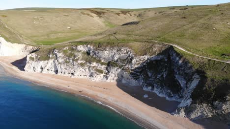 Luftaufnahme-Des-Leeren-Strandes-Neben-Sanften-Hügelklippen-Bei-Durdle-Door-In-Dorset