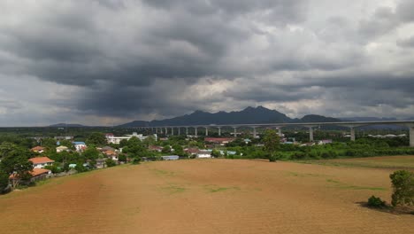 Aerial-footage-of-a-landscape-and-agricultural-fertile-land,-newly-built-elevated-railway-across-town-in-countryside-of-Saraburi-in-Thailand-during-a-cloudy-day-in-the-afternoon