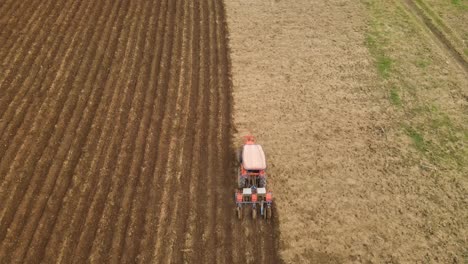 Aerial-footage-capturing-a-piece-of-perfectly-symmetrical-tilled-land,-with-a-busy-farmer-driving-a-tractor-ploughing-the-farmland,-beautiful-contrast-of-soil-pattern-shown-on-the-ground