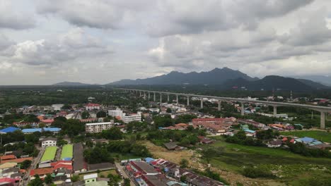 Aerial-footage-sliding-to-the-left-of-Muak-Lek-and-mountains-in-the-horizon,-a-high-speed-elevated-railway-through-the-town-during-a-cloudy-day-in-Saraburi,-Thailand