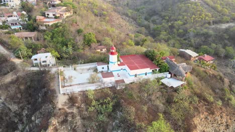Orbital-plane-to-left-with-jib-up,-around-small-lighthouse,-with-view-of-cliff-at-sunrise-in-Oaxaca's-shore