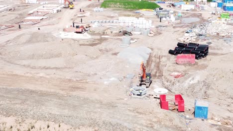 Excavation-digger-vehicle-preparing-concrete-cylinder-pipe-aerial-view-on-housing-development-construction-site