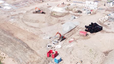 Heavy-construction-machinery-laying-concrete-waste-pipes-on-real-estate-construction-site-aerial-view-descending