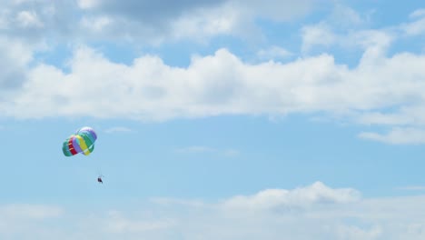 View-of-couple-flying-in-a-parachute-pulled-by-a-boat-over-a-blue-sky-with-white-clouds