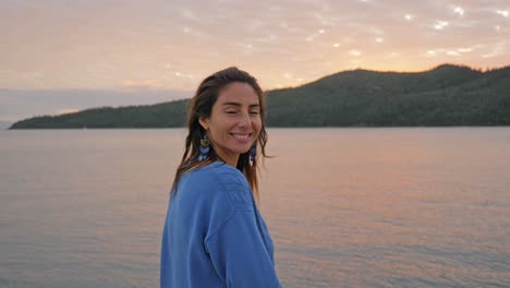 Kaukasisches-Mädchen-Im-Blauen-Pullover,-Das-Sonnenuntergang-Und-Seelandschaft-Bewundert,-Dreht-Den-Kopf-Und-Lächelt-In-Die-Kamera