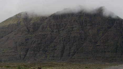Smooth-dolly-out-from-the-cliff-faces-and-mountain-ranges-of-Fjallsárlón-in-Iceland---The-mountain-peaks-are-covered-in-clouds